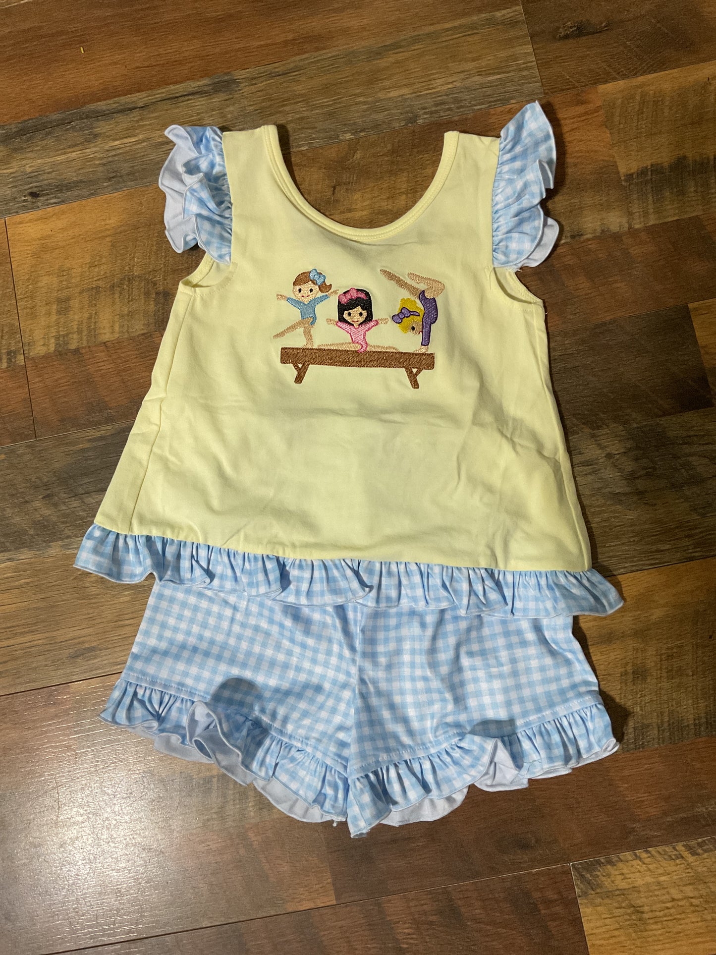 Flippin’ Sweet girls gymnastics short set with yellow embroidered gymnast top and blue gingham ruffle shorts.