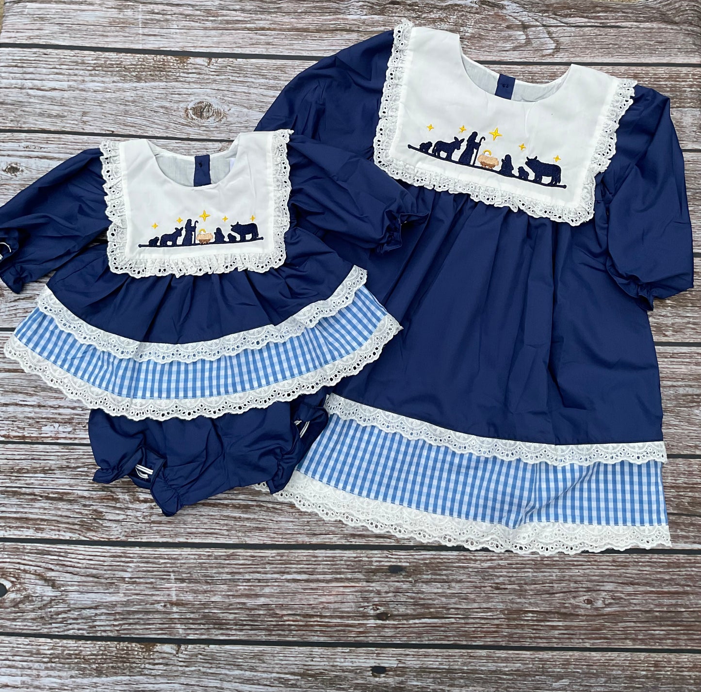 O Holy Night girls nativity dress and bloomer set in navy blue with embroidered nativity scene, white eyelet lace, and blue gingham trim.
