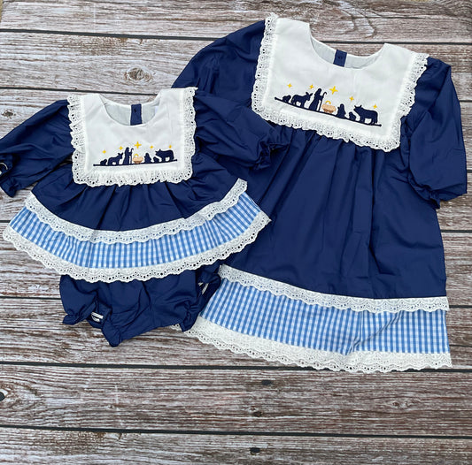 O Holy Night girls nativity dress and bloomer set in navy blue with embroidered nativity scene, white eyelet lace, and blue gingham trim.